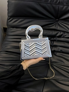 Detail of silver metallic handbag with 3D V-wave texture and gold chain strap