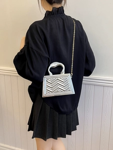 Detail of silver metallic handbag with wave textures and sleek metal handle on a model