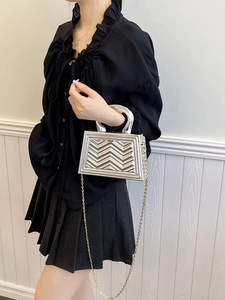 Detail of silver structured bag with 3D chevron pattern and gold metal chain strap