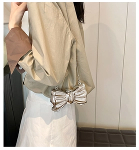 Silver bow-shaped metallic evening bag with sleek chain strap shown on model
