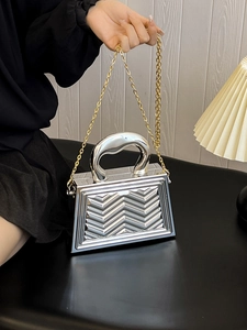 Detail of silver metallic handbag with geometric V-pattern and gold chain strap