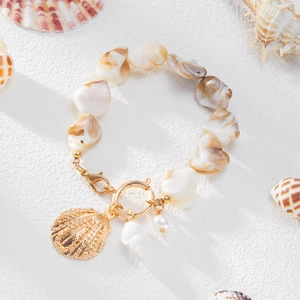 Detail eines Strandarmbands mit Muschelperlen, goldenem Jakobsmuschel- und Schneckenanhänger