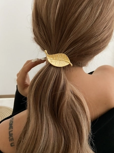 Detailed view of a golden leaf-shaped metal hair clip on a low ponytail hairstyle