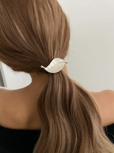 Detailed view of silver metal leaf hair clip on long brown hair in a ponytail style