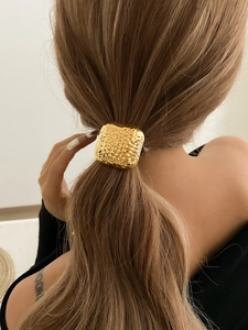 Close-up of golden square hair tie with hammered metal texture for ponytail styling