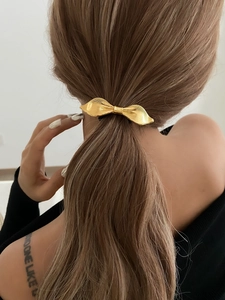 Detail of elegant gold metal bow hair clip with brushed texture on low ponytail