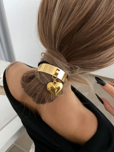 Detailed view of polished gold heart pendant hair tie worn on a messy bun hairstyle