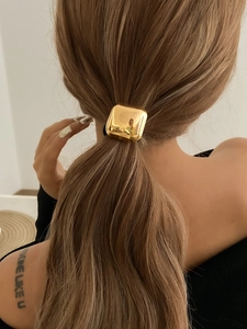 Close-up of a polished golden square metal hair tie on a woman's brown ponytail