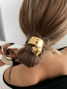 Detail of a golden heart pendant hair tie with a polished metal cuff on a ponytail