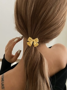 Close-up of golden bow hair tie with textured finish on a high ponytail style