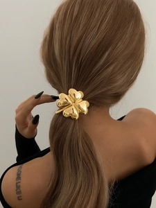Close-up of a golden four-leaf clover ponytail holder in a long blonde hair setting