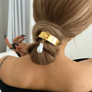Close-up of golden metal hair buckle with baroque pearl pendant on a hair bun