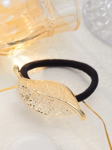 Close-up of a golden metal leaf hair tie with detailed texture on a white tray