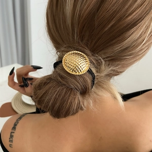 Detail of a textured golden circular metal charm on a black high-elasticity hair tie