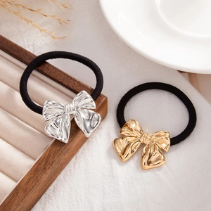 Detailed macro of gold and silver metallic bow hair ties on a rustic wooden stand