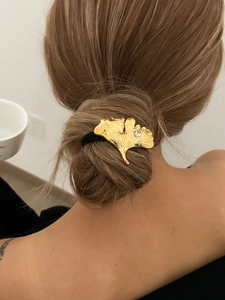 Detail van een gouden ginkgo blad haarelastiek met een kristal op een zwarte elastische band
