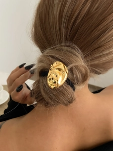 Détail d'un anneau de cheveux en métal doré au style lave sur un élastique noir pour queue
