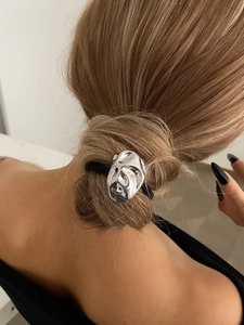 Détail d'un élastique à cheveux en métal argenté avec design fluide sur une queue de cheval