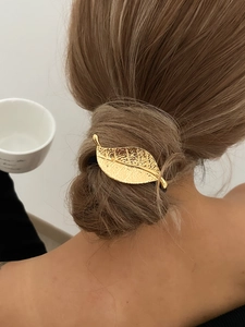 Gros plan d'une pince à cheveux feuille dorée avec textures sur un chignon brun