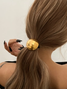 Detail of faceted gold disco ball elastic hair tie securing a brunette ponytail