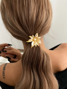 Detailed view of a gold leaf ponytail clip with pearl accent on a model's hair