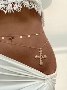 Detail of bohemian gold waist chain with intricate embossed cross pendant and colorful gems