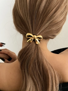 Detailed back view of a golden metallic bow hair tie styling a low ponytail hairstyle