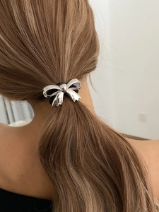 Close-up of a silver bow ponytail holder with a metallic finish on a low ponytail hair