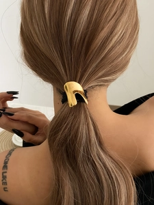 Close-up of a minimalist gold metal ponytail cuff with irregular geometric design and elastic band
