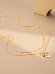 Detail of layered gold snake chain necklace featuring a delicate bow pendant decoration