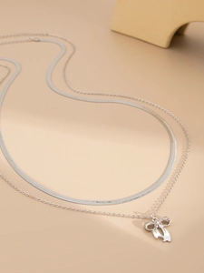 Detail of silver double-layered necklace featuring a flat herringbone chain and bow pendant