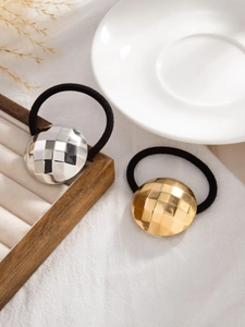 Macro shot of geometric faceted gold and silver ponytail holders on white textured fabric