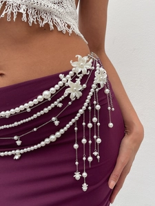 Detail of layered pearl body chain with floral accents and silver tassels on garment