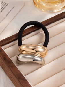 Macro detail of irregular wave metal hair tie on a beige velvet jewelry display tray