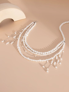 Detail of layered white pearl body chain with silver tassels on a warm beige background