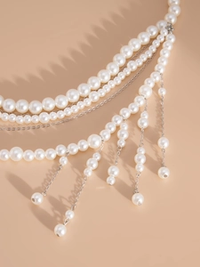 Detail of layered pearl body chain with silver tassels on a neutral background