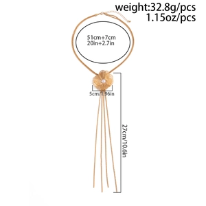 Détail d'un collier fleur doré avec pétales ajourés, perle et longues franges en métal