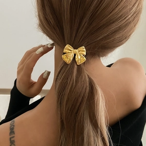 Elegant gold bow hair tie with textured finish on ponytail, minimalist fashion accessory
