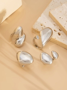 Dettaglio macro di 4 anelli impilabili in argento lucido con design organici in metallo fluido