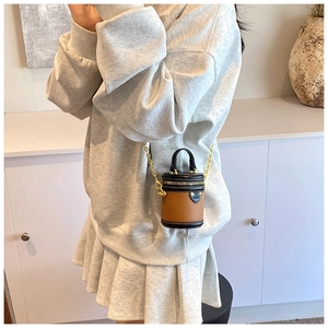 Mini brown and black cylinder bucket bag with chain strap worn by a model in casual setting