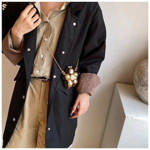 Detailed view of flower-shaped crossbody bag with gold petals and white pearl on the model