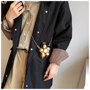Macro shot of gold flower crossbody bag with pearl center and metallic finish on black coat