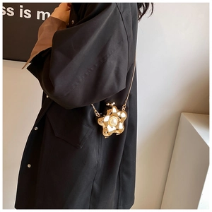 Detail view of a gold flower-shaped crossbody bag with central pearl and elegant chain