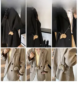 Mini borsa a tracolla metallica a forma di conchiglia indossata su cappotto nero e blazer marrone