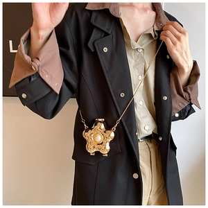 Fashionable gold star-shaped crossbody bag with pearl detail worn by model over black coat