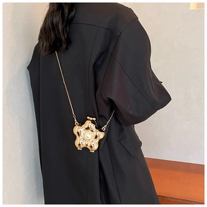Detail of a golden flower evening bag with a pearl center and sleek metal chain strap