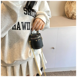Detail of mini bucket bag in black pebbled leather with gold hardware and chain strap