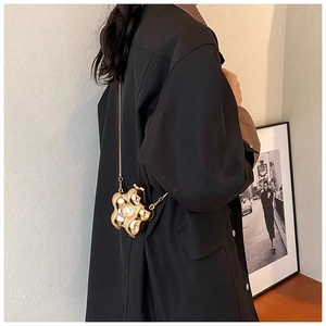 Detail of a golden flower evening bag with a central pearl and fine chain strap