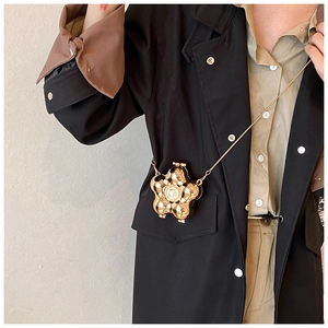 Chic gold flower mini bag with pearl center and chain strap worn on black trench coat
