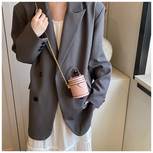 Detailed view of pink mini cylinder crossbody bag with gold chain strap on female model
